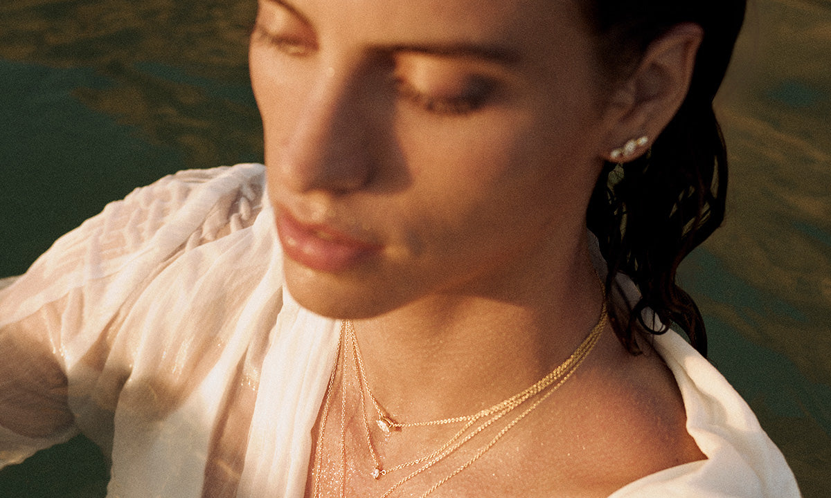 Model in natural light emerging from water, wearing ANNOORY layered gold necklaces with lab grown diamonds and matching diamond earrings, embodying elegance and fluidity.